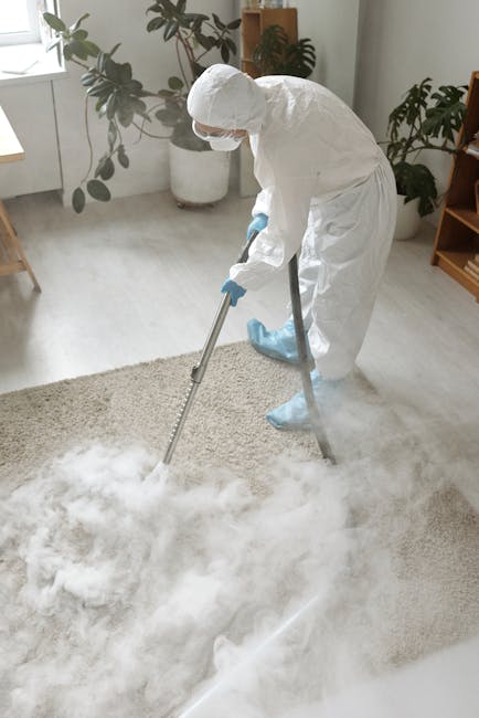 Two professional cleaning technicians from Ilford Carpet Cleaners are preparing equipment outdoors beside a white vehicle. Both are dressed in red and gray uniforms with caps, and one is handling a ye
